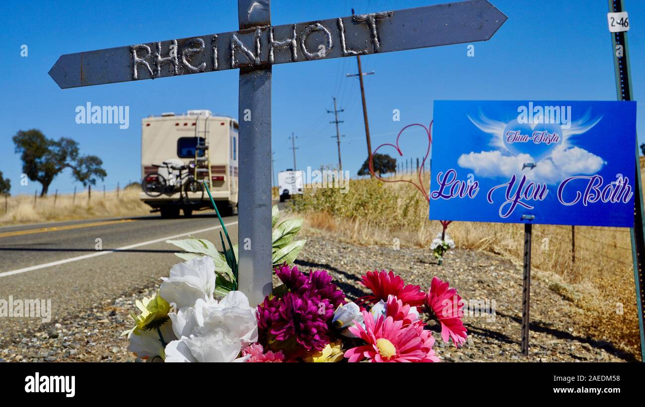 Roadside car accident memorial with a metal cross with the name Rheinholt, with recreational vehicles driving by in Tuolumne County, California. Stock Photo