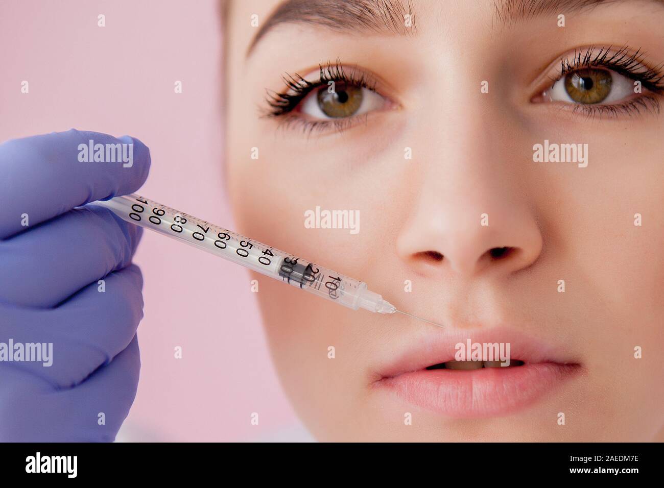 Doctor in gloves giving woman botox injections in lips, on pink ...