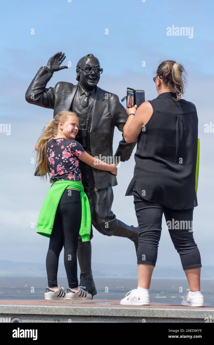 Mother and daughter posing by Eric Morecambe statue on beach promenade