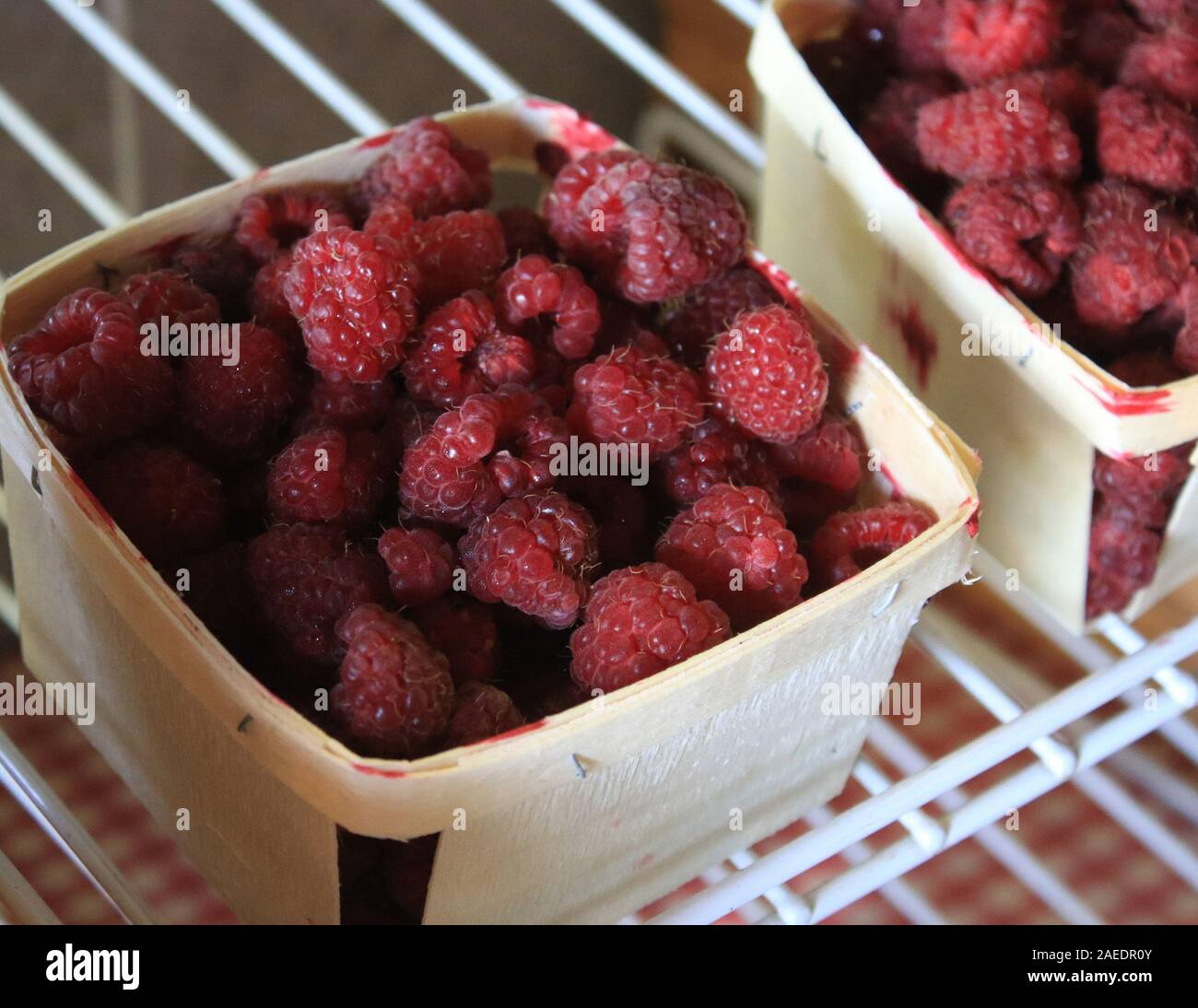 Red raspberries are seen in a wooden quart container on a shelf Stock ...