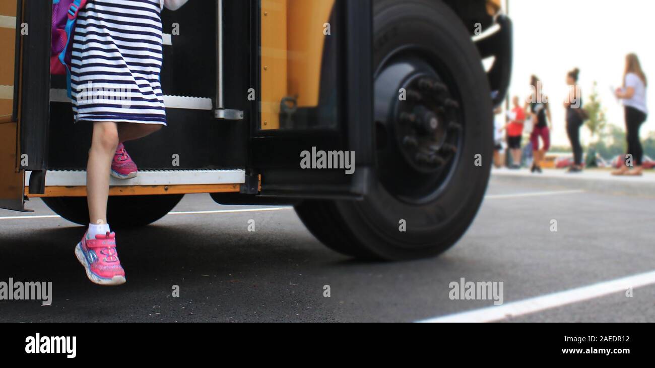 A female student steps off a school bus for the first day of school in this photograph. Stock Photo