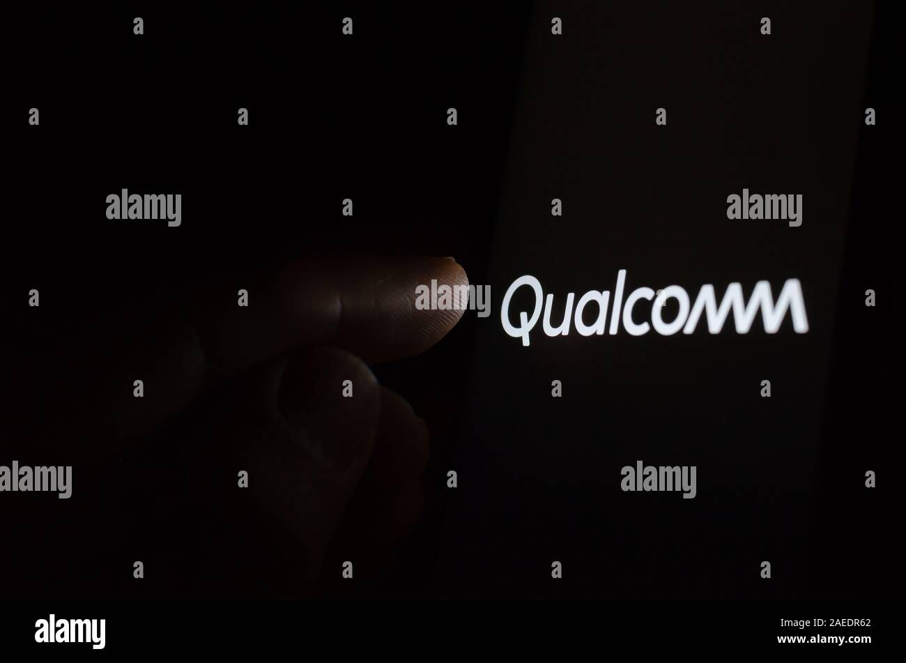 Qualcomm logo on a glowing screen and a hand pointing at it. Stock Photo