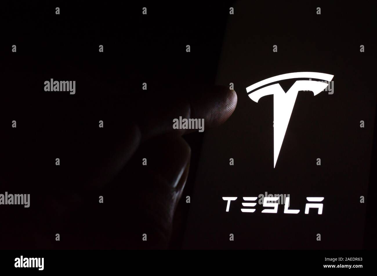 Tesla car logo on a glowing screen and a hand pointing at it. Stock Photo