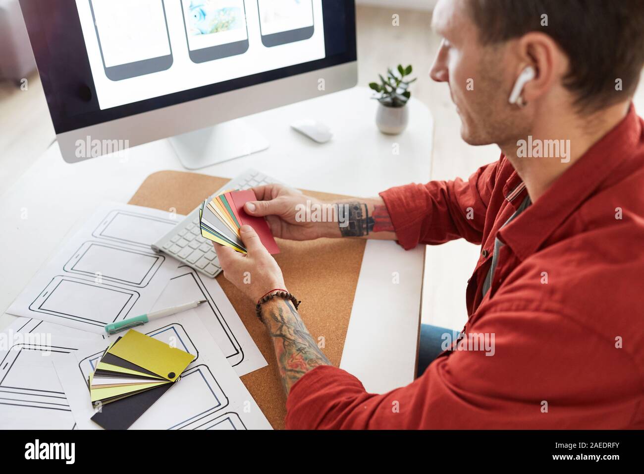 High angle portrait of tattooed man holding color samples while choosing palette for web design project, copy space Stock Photo