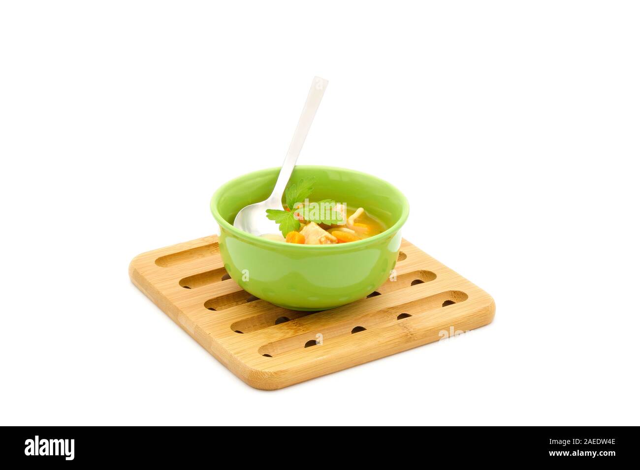 Bowl of Chicken noodle soup in a green bowl sitting on a wooden trivet photographed on a white background. Stock Photo