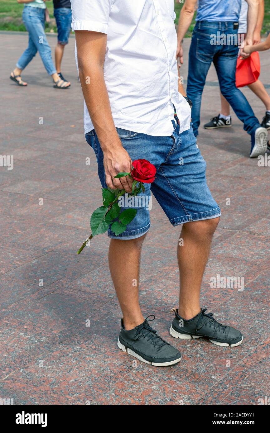 A young man with a flower in hand is waiting for a loved one to come. Part of a man's body. Summer, on the street. Stock Photo