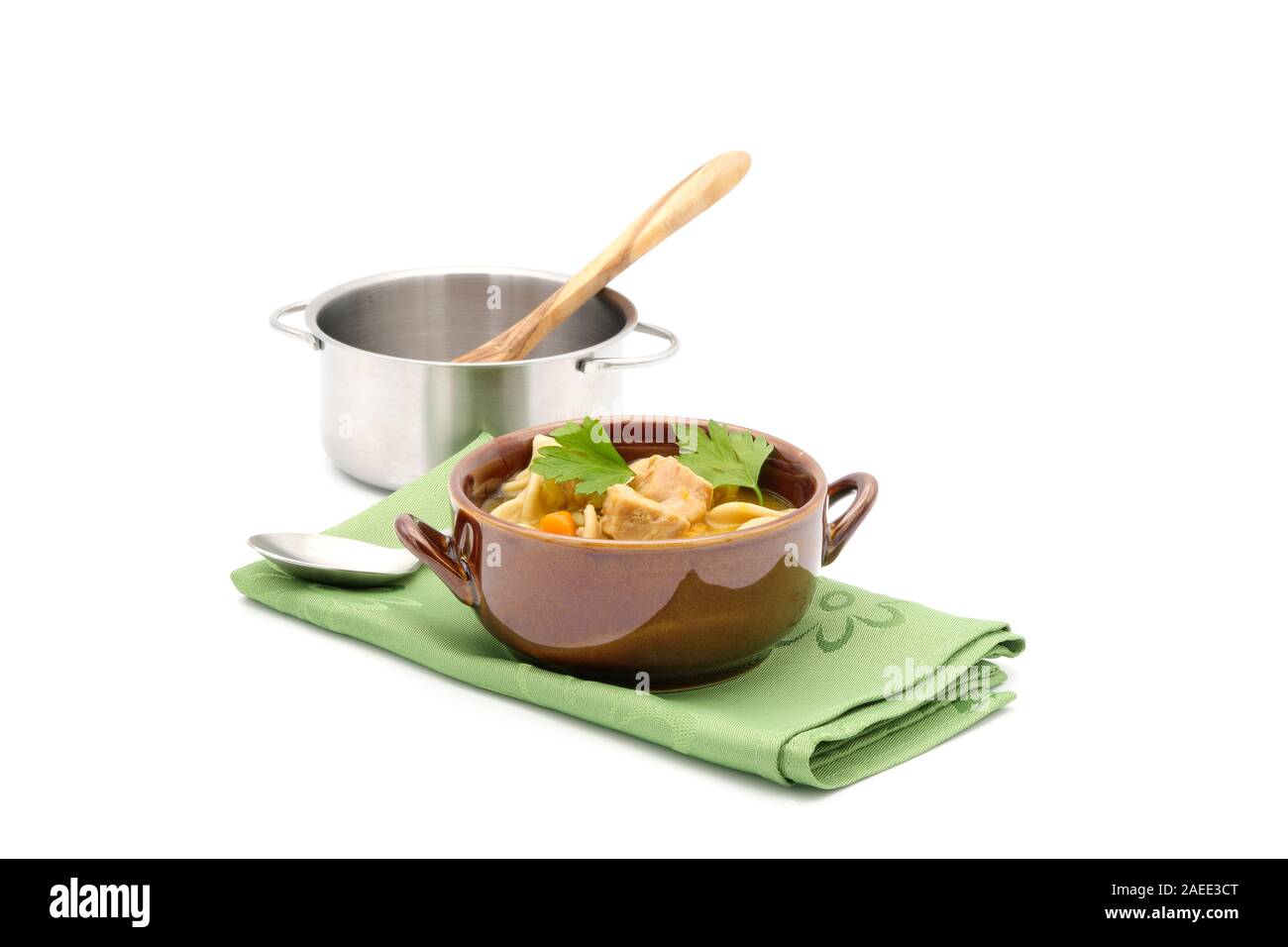 Bowl of Chicken noodle soup in a brown bowl sitting on a  green napkin photographed on a white background. Stock Photo