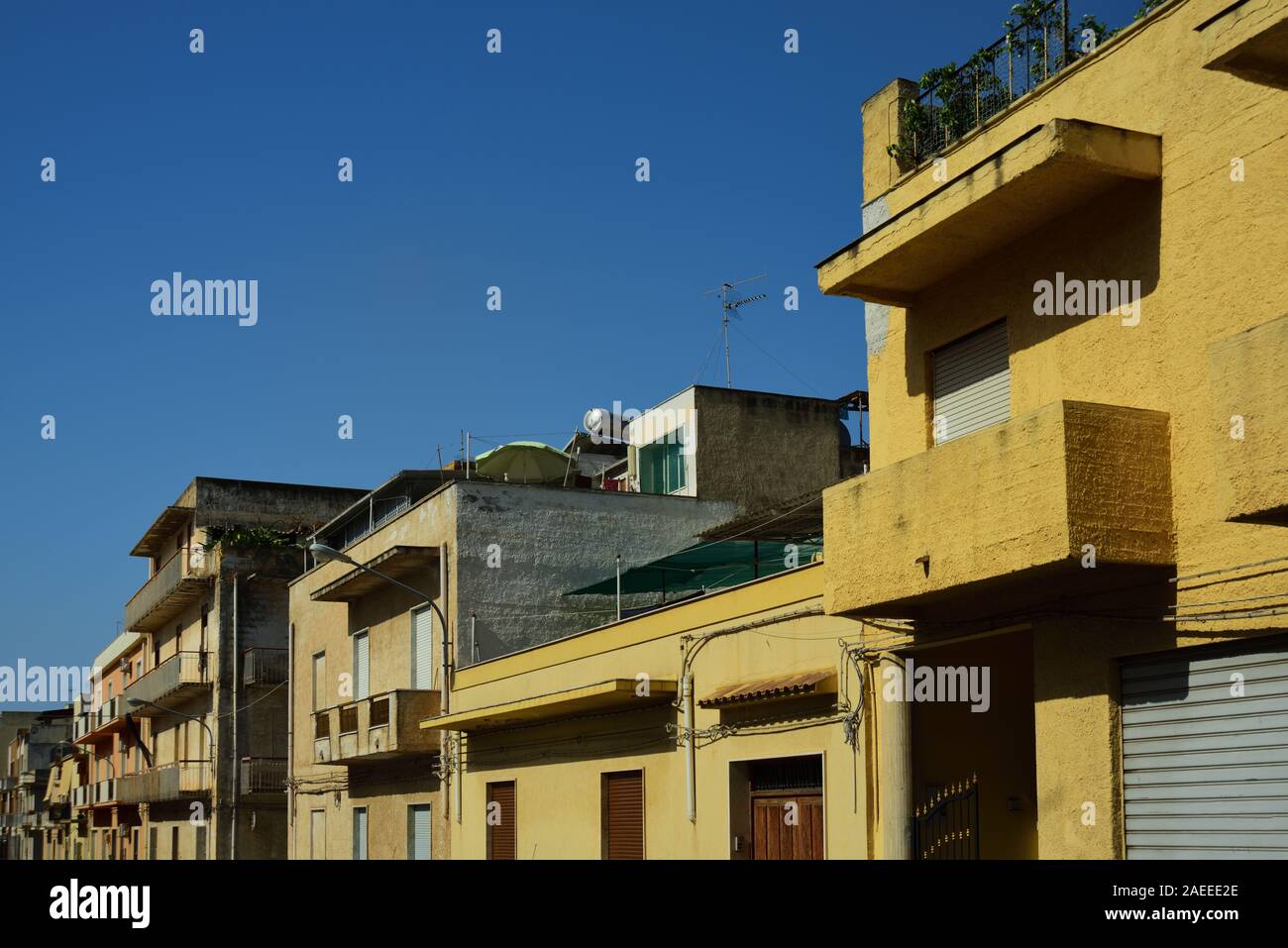 Typical row of flat houses in the middle of a city at the roadside on Sicily in Italy in summer with closed windows against blue sky in the heat of th Stock Photo