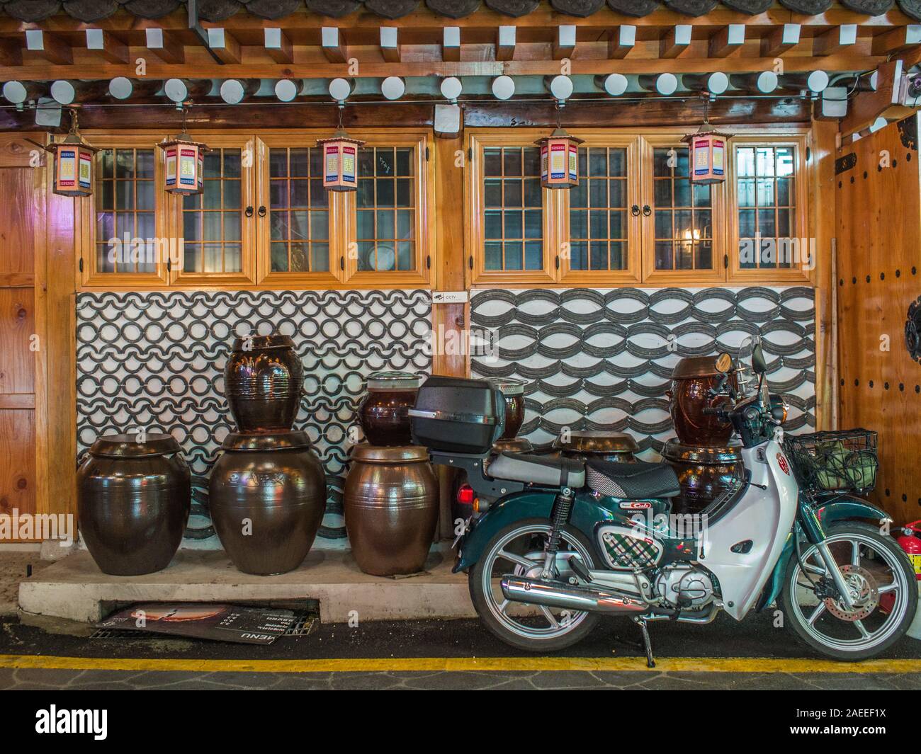 Honda Super Cub motorbike, parked outside traditional hanok house, decorative tile wall,  pickling jars, Gyeongbokgung,  Seoul South Korea Stock Photo