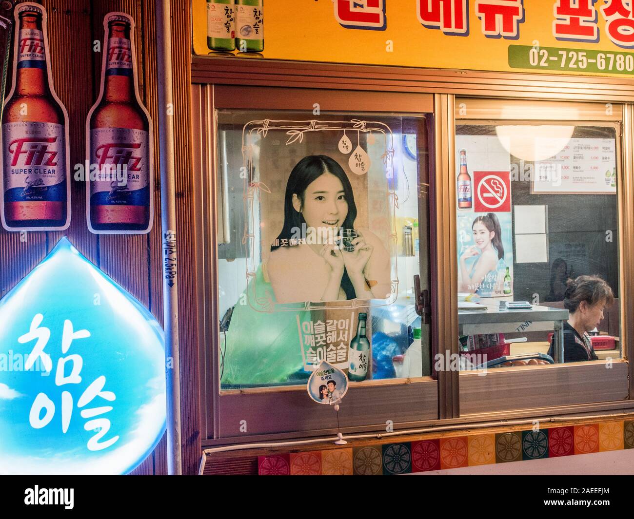 Restaurant window, alcohol liquor advertisments featuring young women, woman worker asleep inside, night street, Gyeongbokgung,  Seoul, South Korea Stock Photo