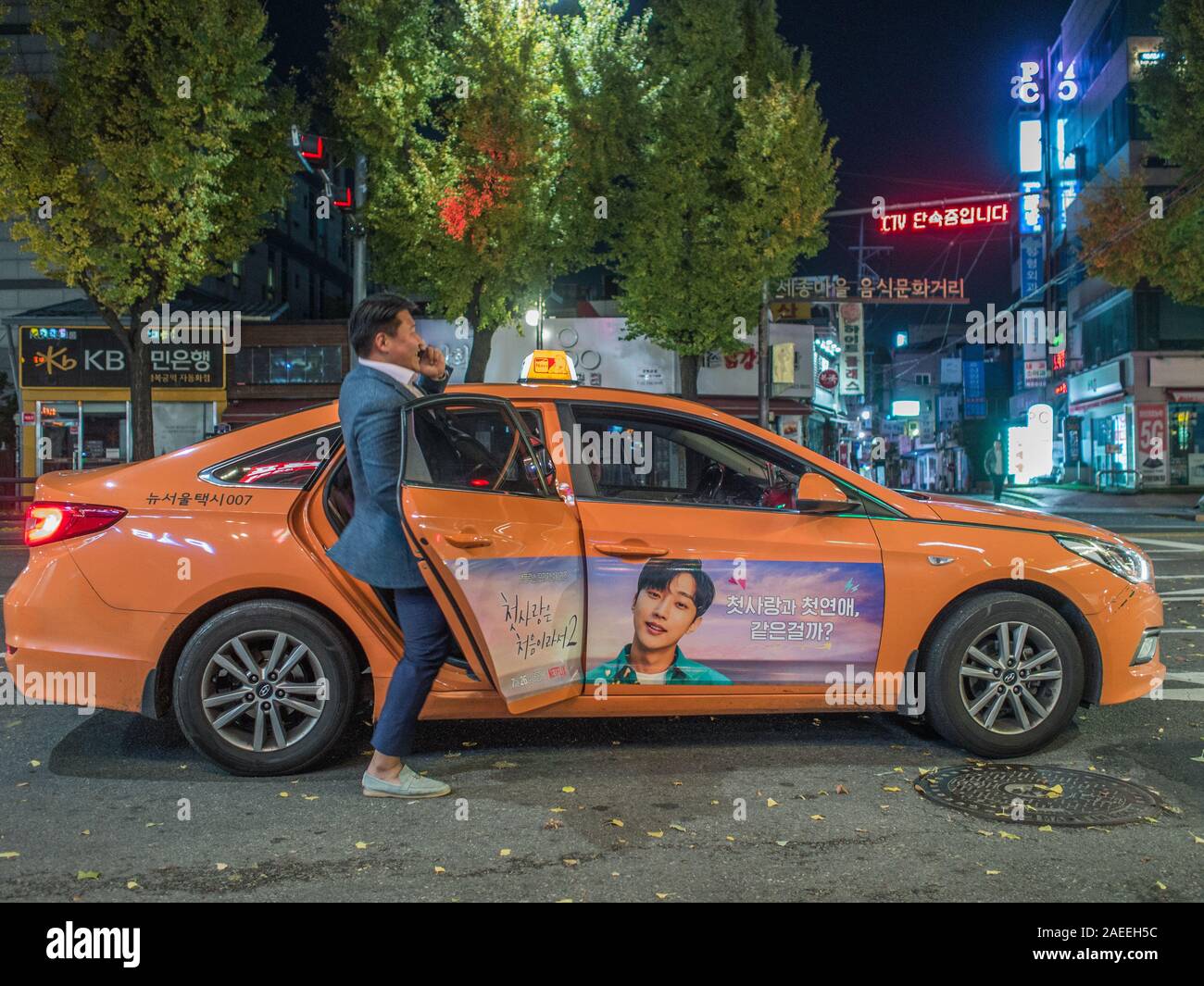 One man, talking on smart phone, getting into orange taxi, near Gyeongbokgung station, night street, Seoul, South Korea. Stock Photo