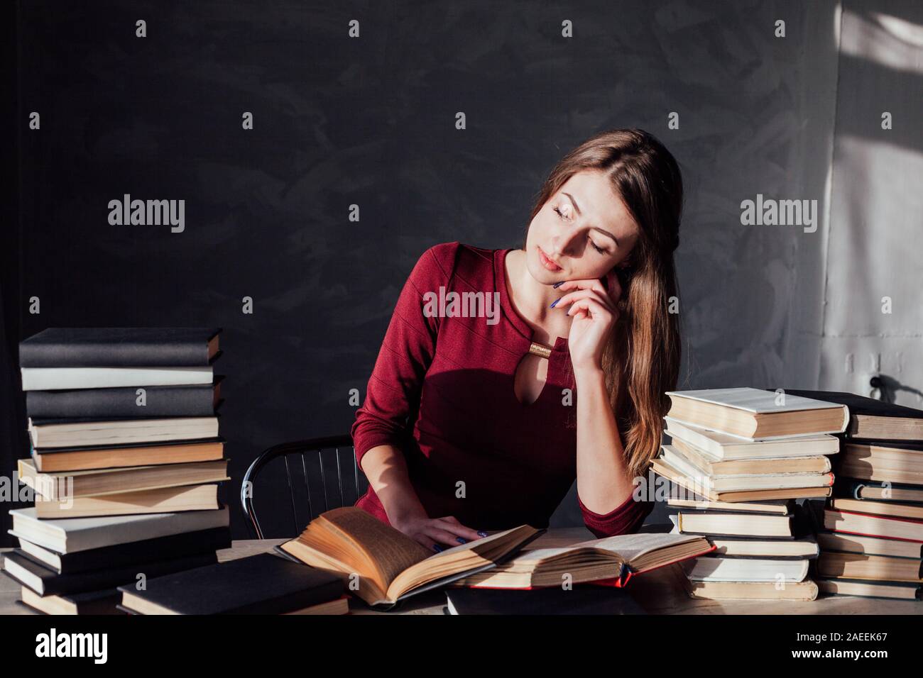 the girl sitting at the table reading a lot of books Stock Photo
