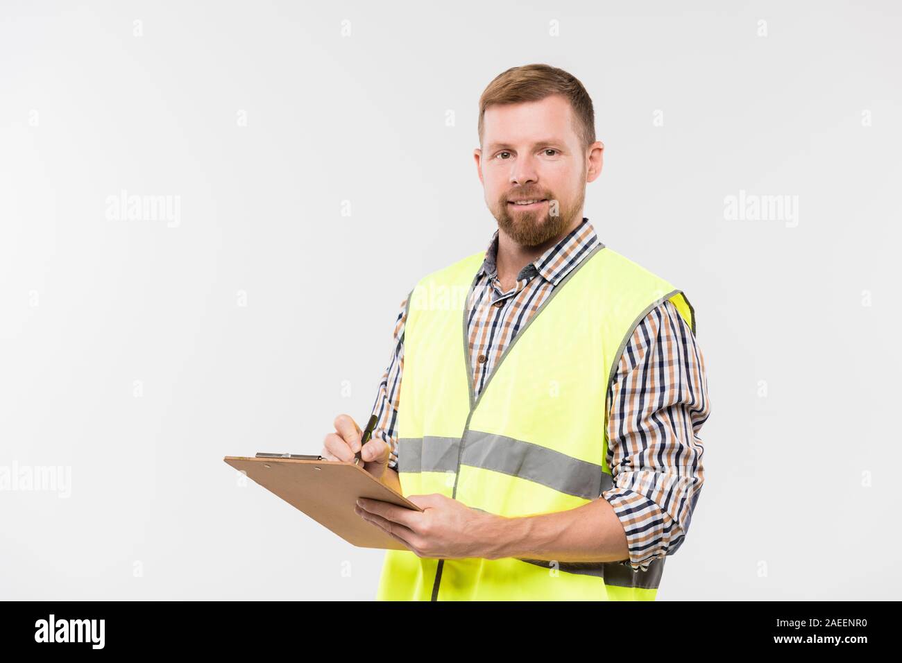 Happy young bearded engineer with clipboard and pen making working notes Stock Photo