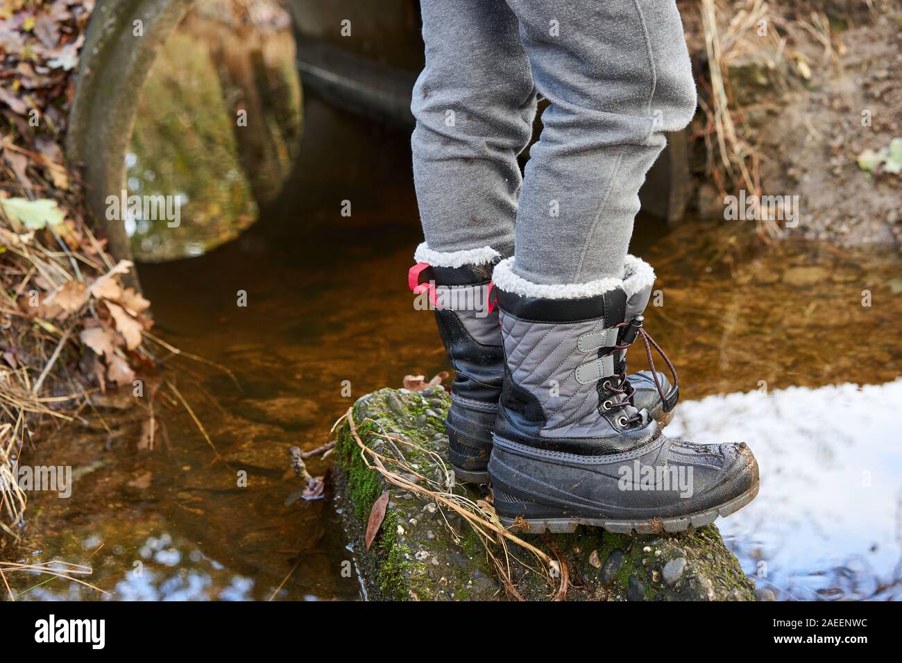 Legs of a boy in grey pants and winter boots standing on a rock in a creek in a local park on a cool autumn day in Windsor, California. Stock Photo
