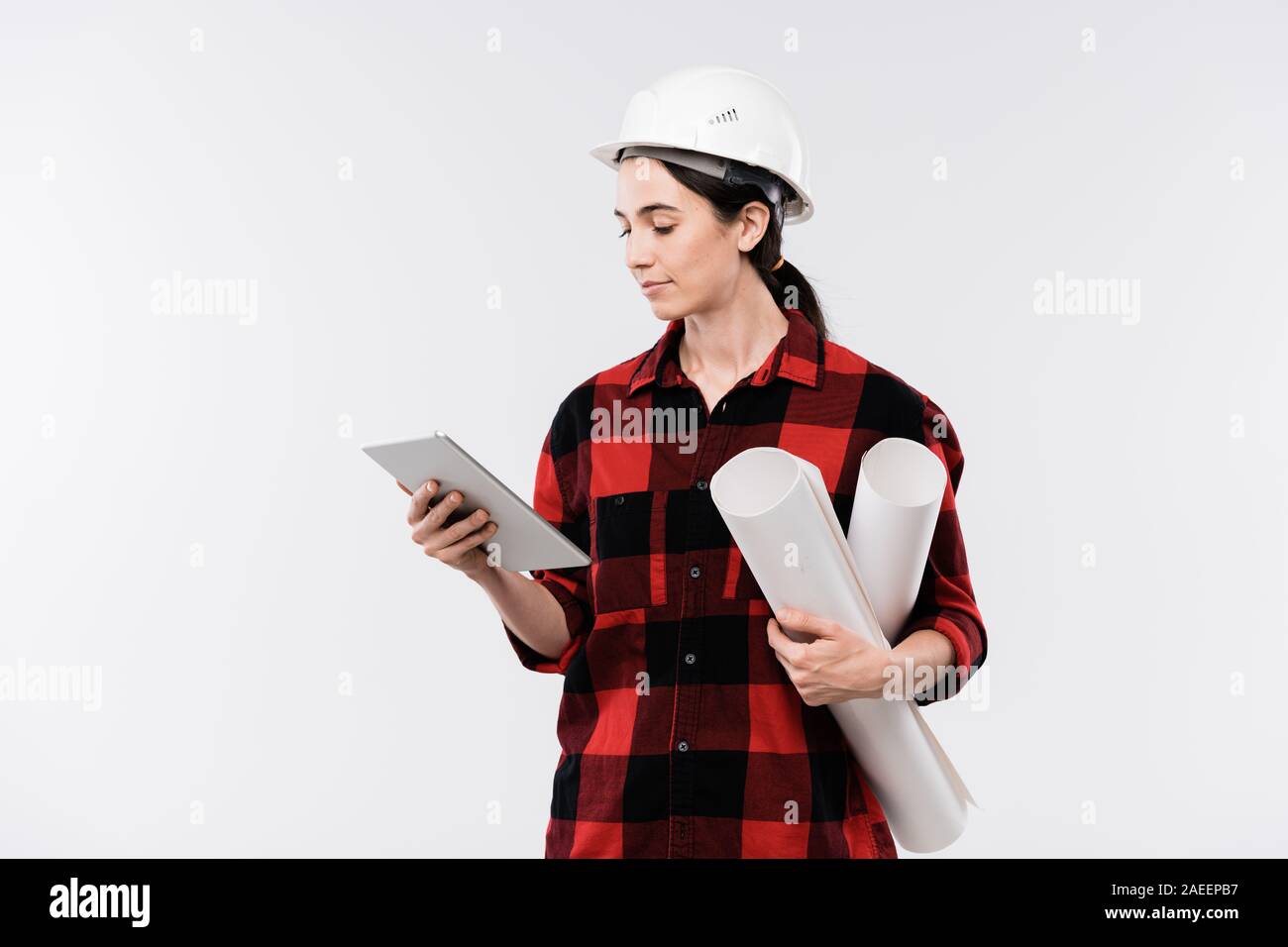 Young serious female engineer in workwear and protective helmet using
