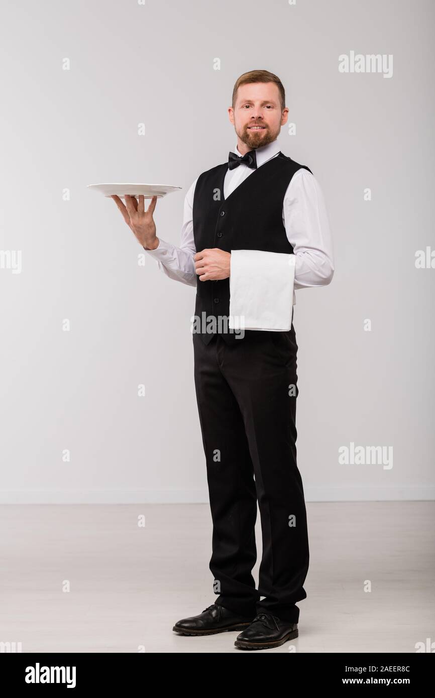 Happy young waiter in elegant suit and bowtie holding white towel and plate Stock Photo