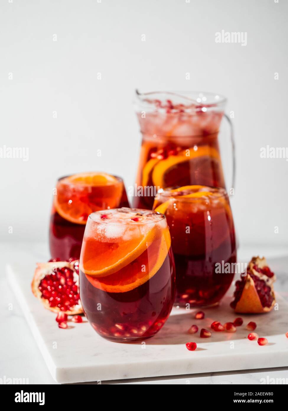 Winter sangria on white marble background. Jugful of sangria and glasses with orange slice and pomegranate. Copy space for text or design. Vertical. Stock Photo
