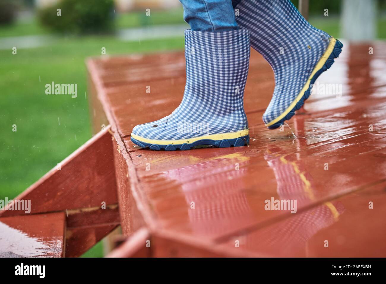 Boy in blue rubber boots down the wet slippery stairs in rainy day