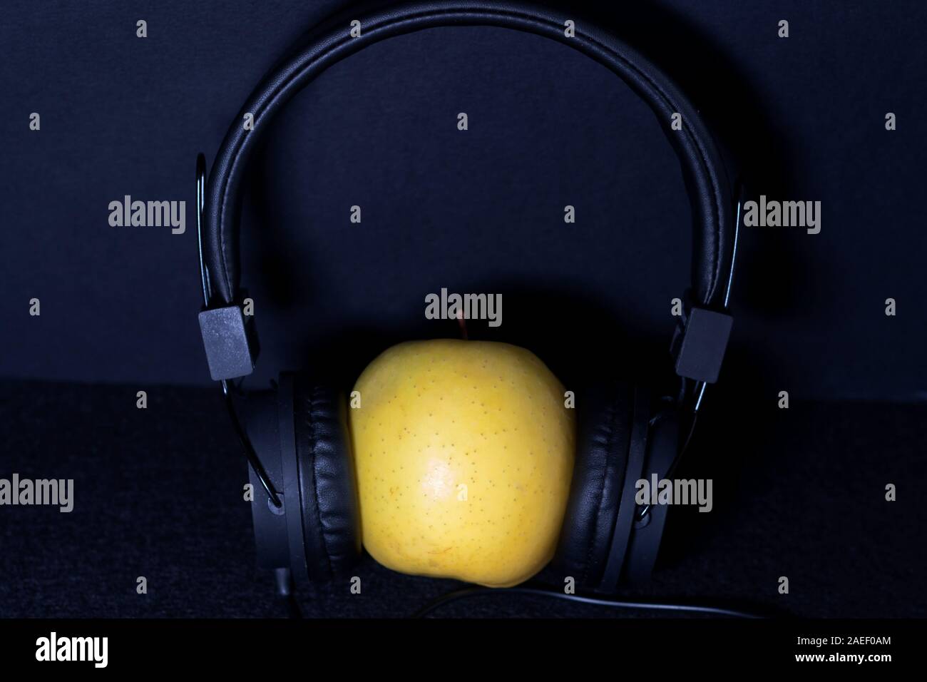 yellow apple wearing black headphones on a dark background. listening music concept. Stock Photo