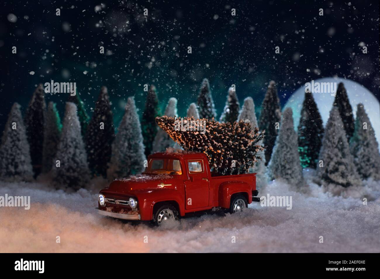 A toy red Chevrolet pickup truck carries a Christmas tree in the forest