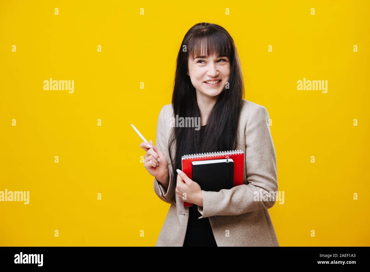 Smiling young business woman in a gray jacket holding pen over yellow Stock Photo