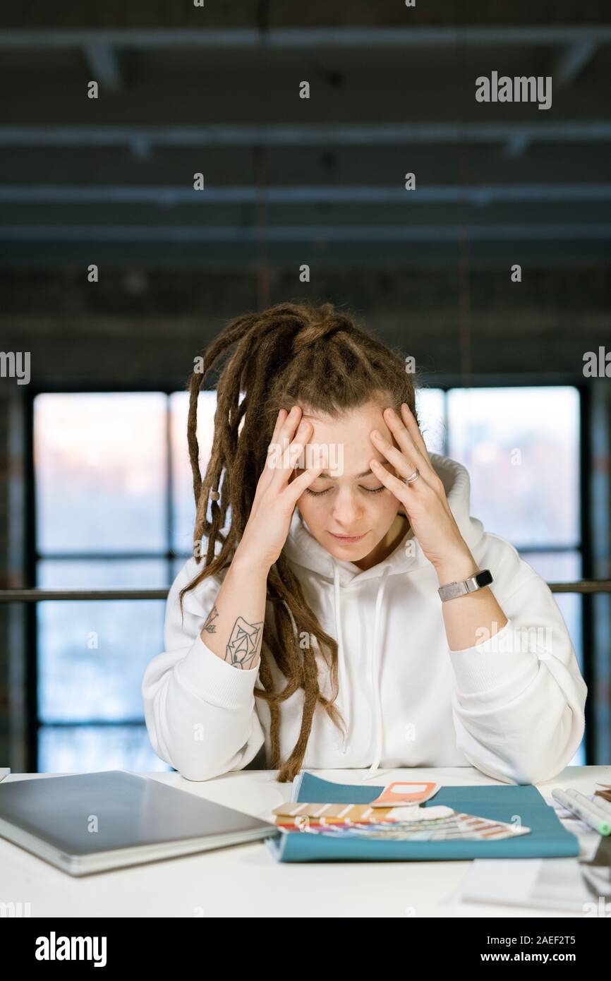 Pensive female designer touching her head while concentrating on work Stock Photo