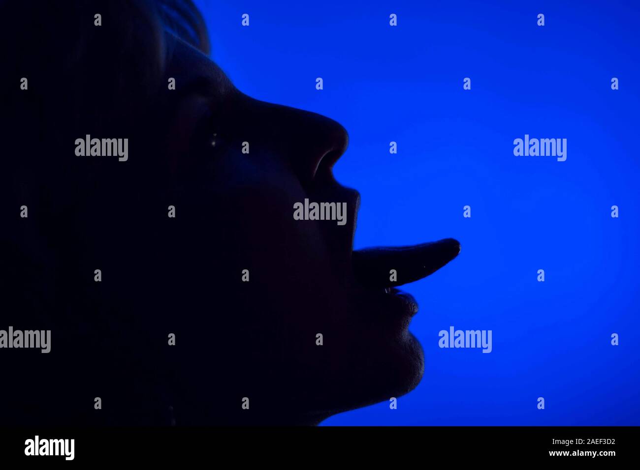 Woman's face showing tongue silhouette in front of blue background Stock Photo