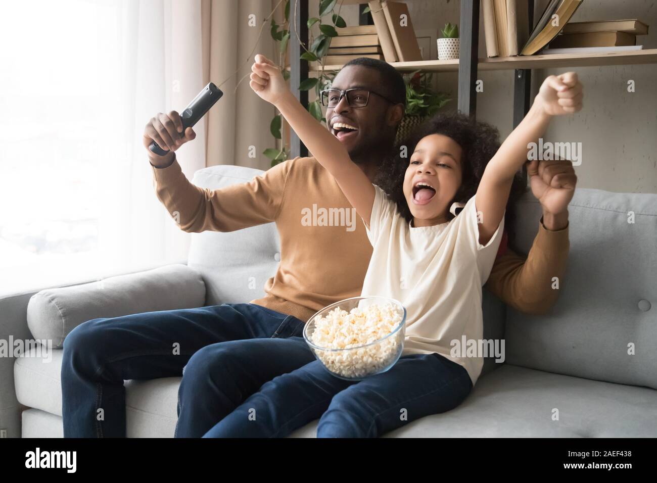 Happy black dad and daughter cheering watching football on TV Stock