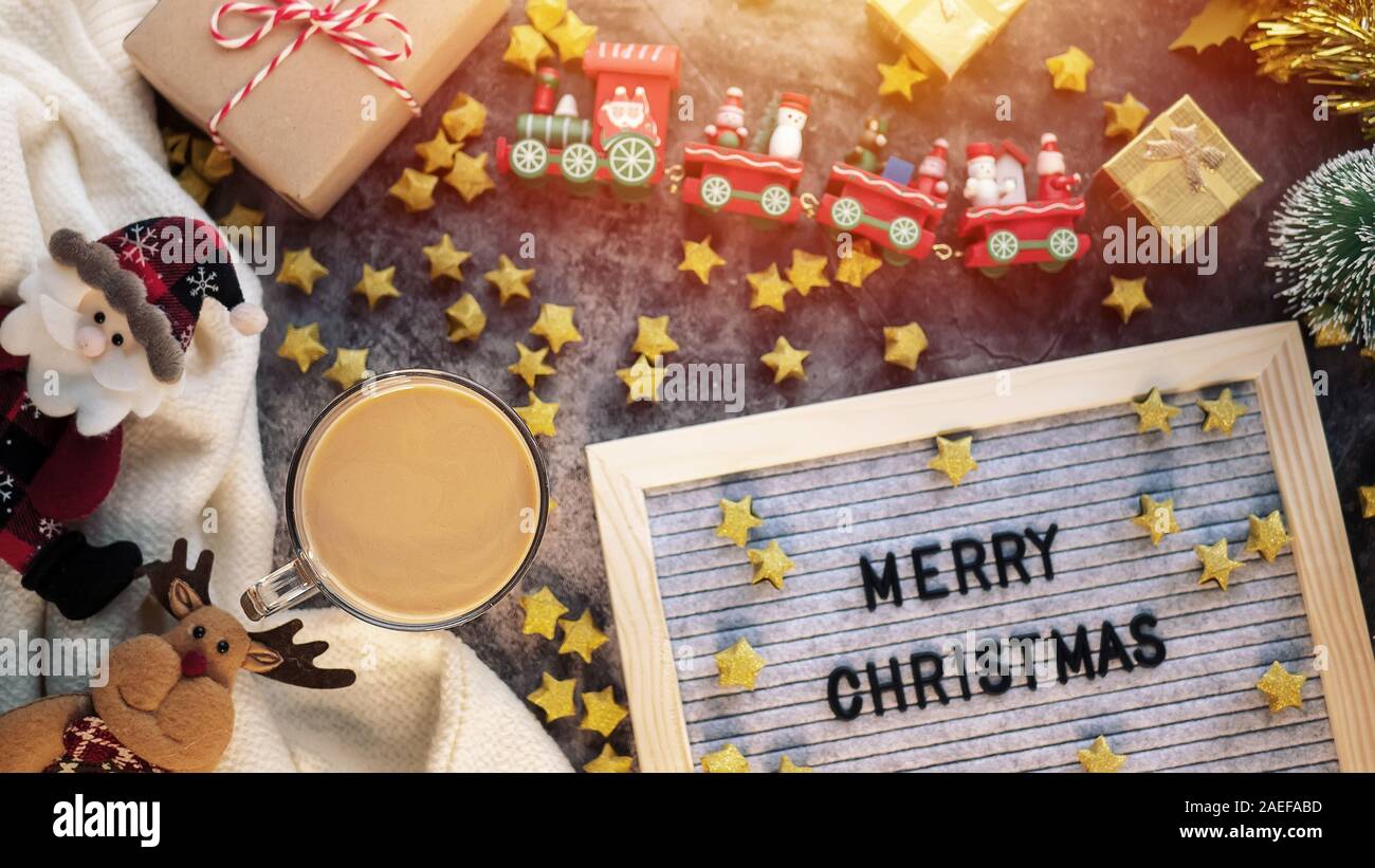 a cup of hot coffee in winter season with text Merry Christmas on letter board , Christmas ornament decorations and gift box on table for Christmas ba Stock Photo