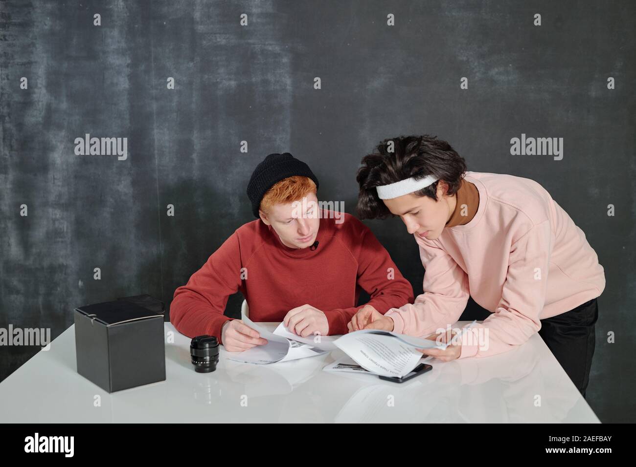 Two young men by desk looking through papers while preparing for video ...