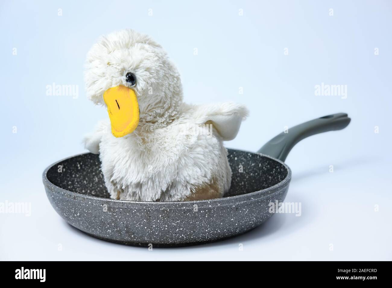 Cute fluffy toy chicken on a frying pan. Cruel meat industry, poultry consumption concept Stock Photo