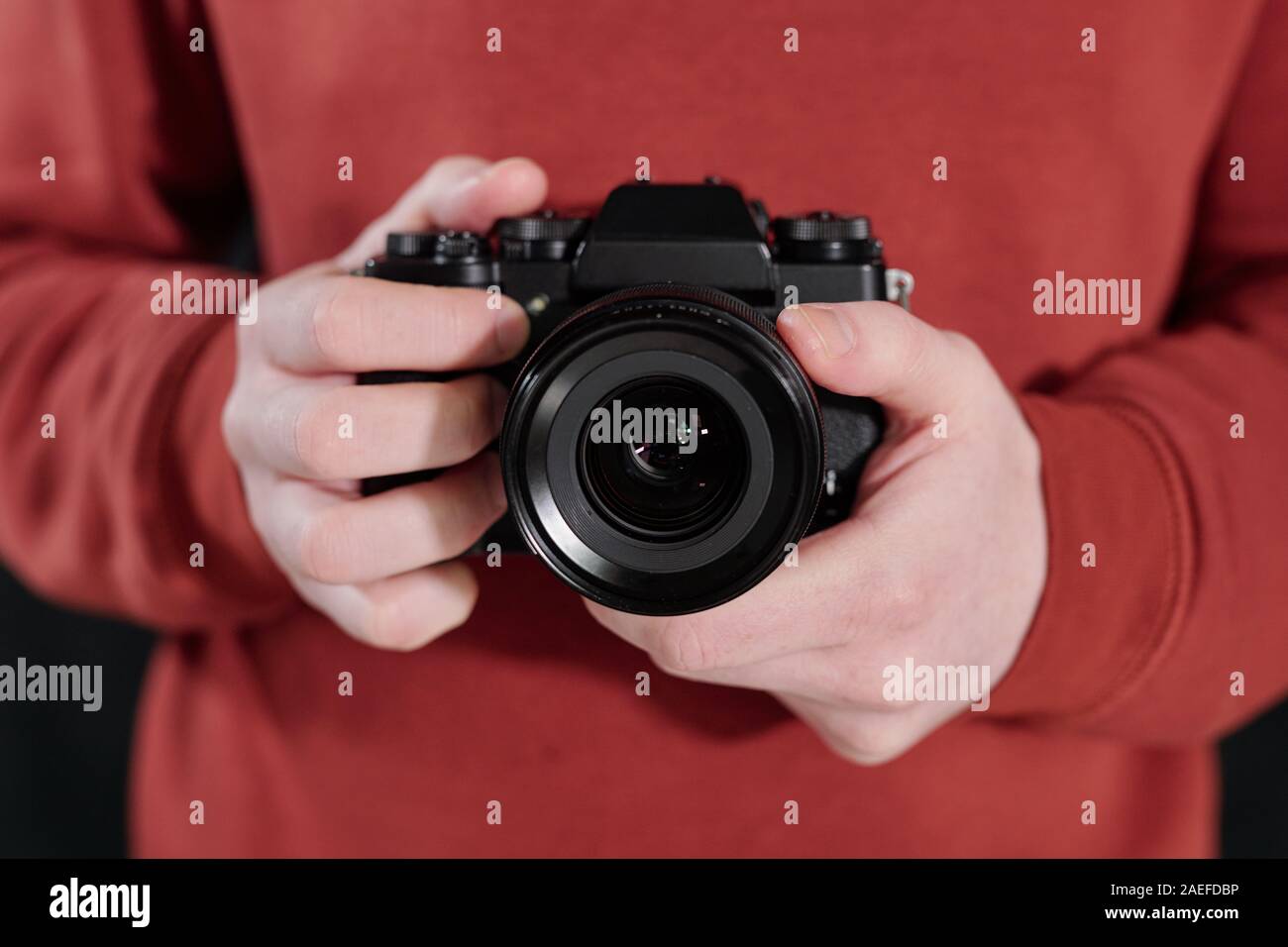 Hands of young male photographer in maroon sweatshirt holding new photocamera Stock Photo