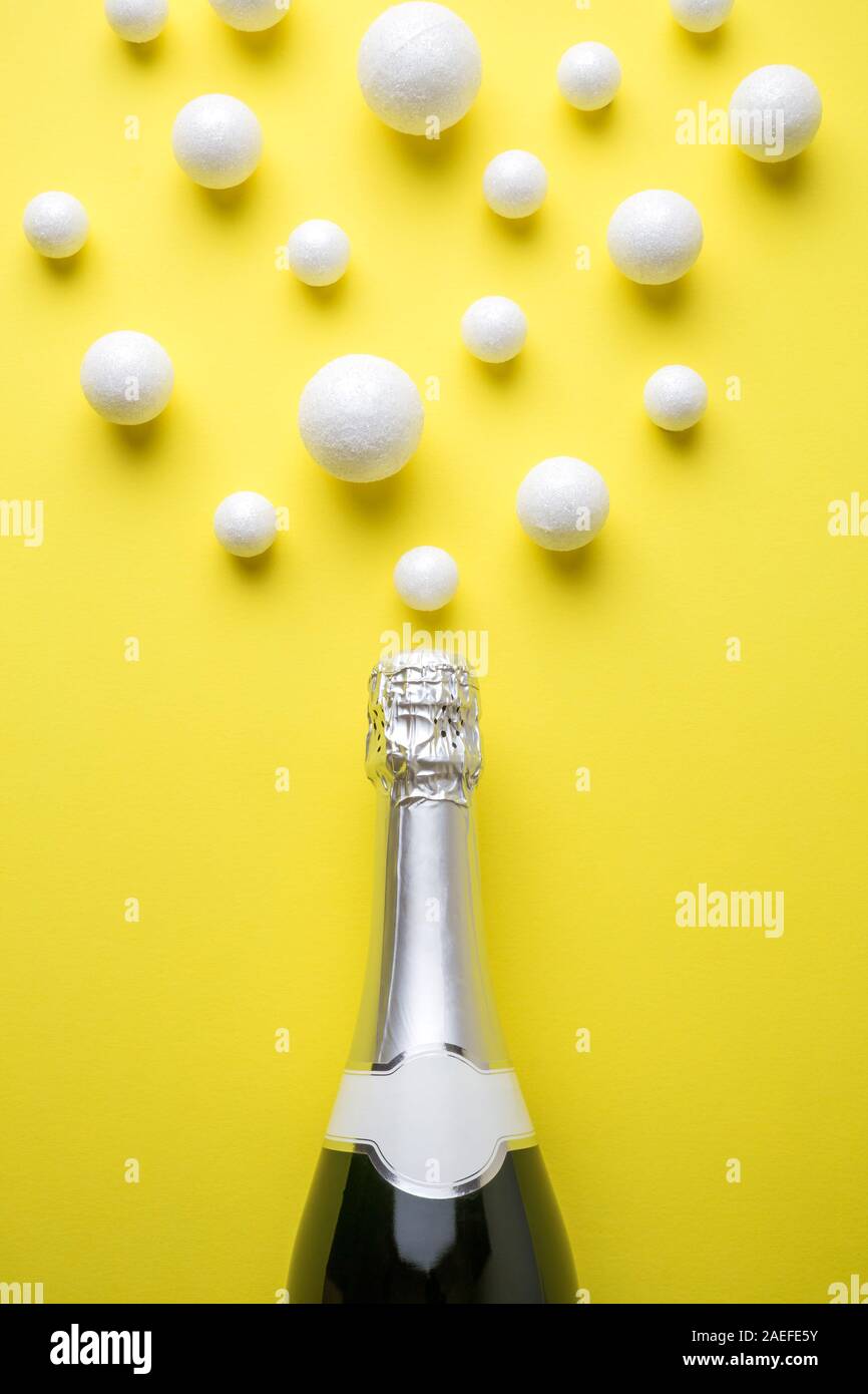 Flat lay of champagne bottle and bubbles made of styrofoam balls against yellow background minimal creative drink concept. Stock Photo