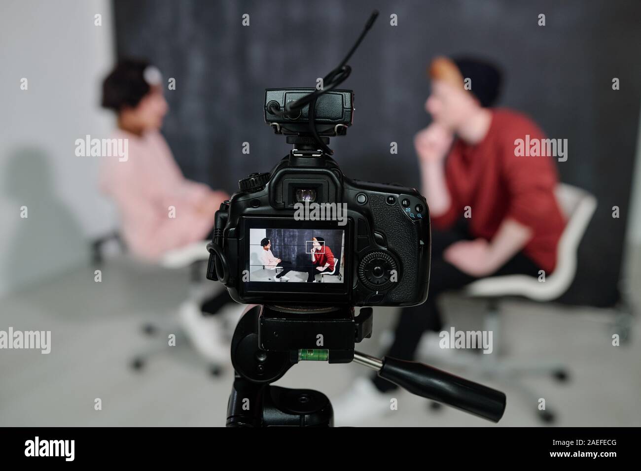 Screen of digital video camera with two vloggers sitting on chairs and