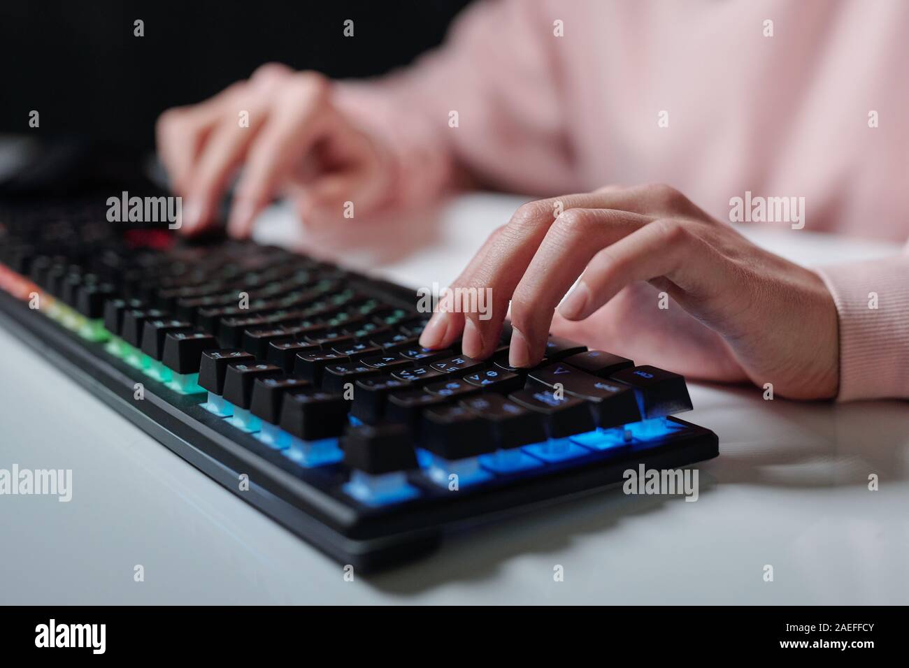Hands of teenager over keys of computer keyboard typing while sitting by desk Stock Photo