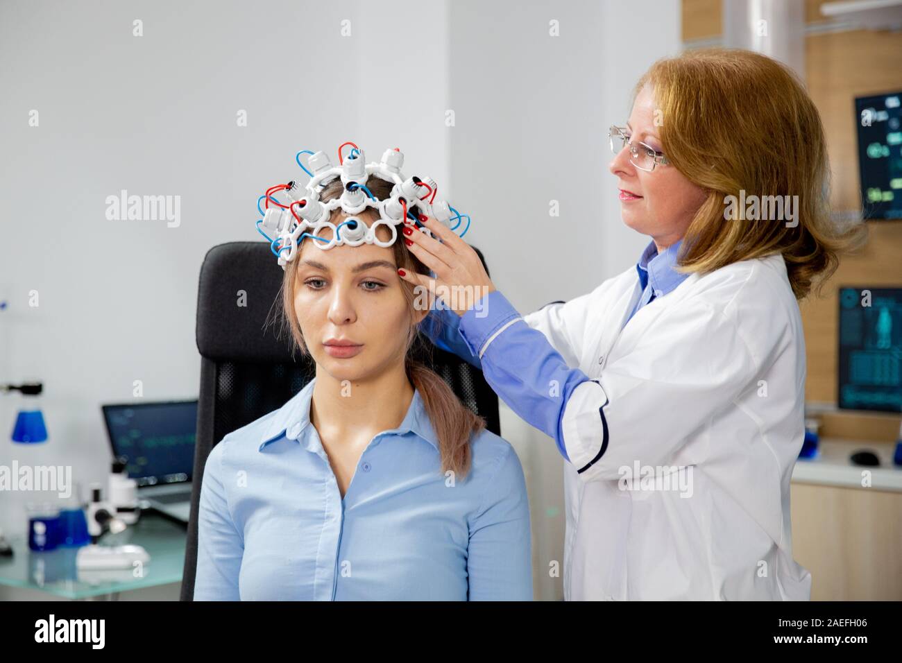 Female scientist who puts brain waves scanning helmet on a female patient. Modern divice and technology Stock Photo