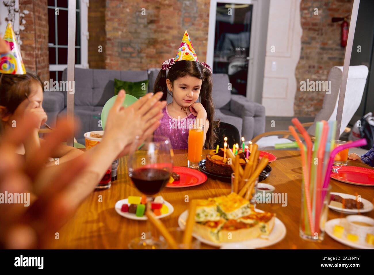 Little happy girl celebrating a birthday at home. Friends eating cake and drinking juice while greeting and having fun children. Celebration, family, party, home, childhood, parenthood concept. Stock Photo