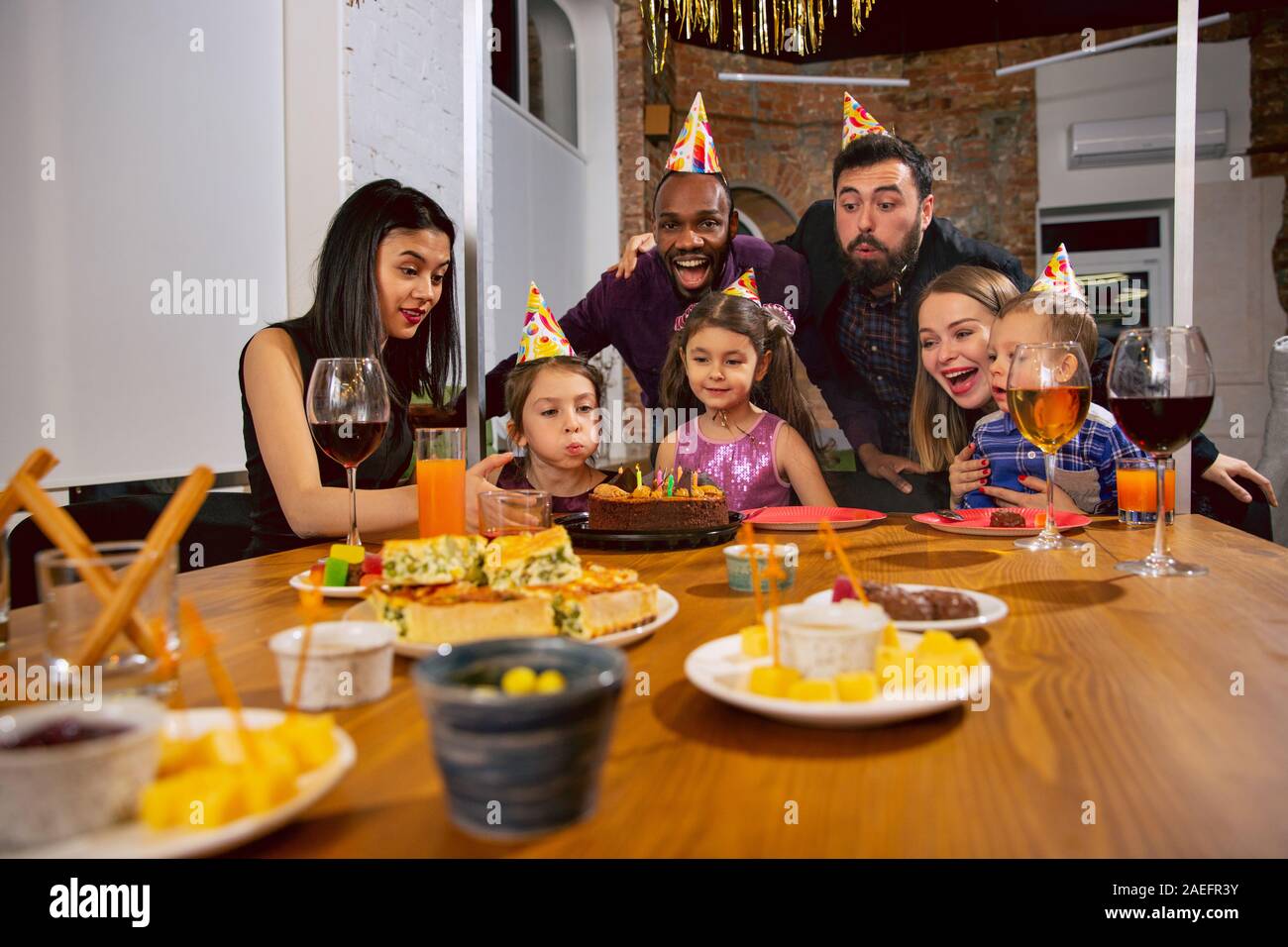 Portrait of happy multiethnic family celebrating a birthday at home. Big family eating snacks and drinking wine while greeting and having fun children. Celebration, family, party, home concept. Stock Photo