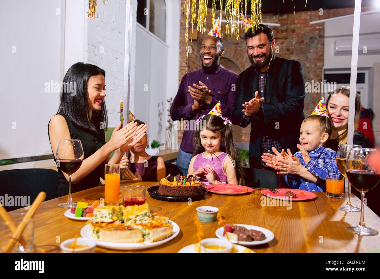 Portrait of happy multiethnic family celebrating a birthday at home. Big family eating cake and drinking wine while greeting and having fun children. Celebration, family, party, home concept. Stock Photo