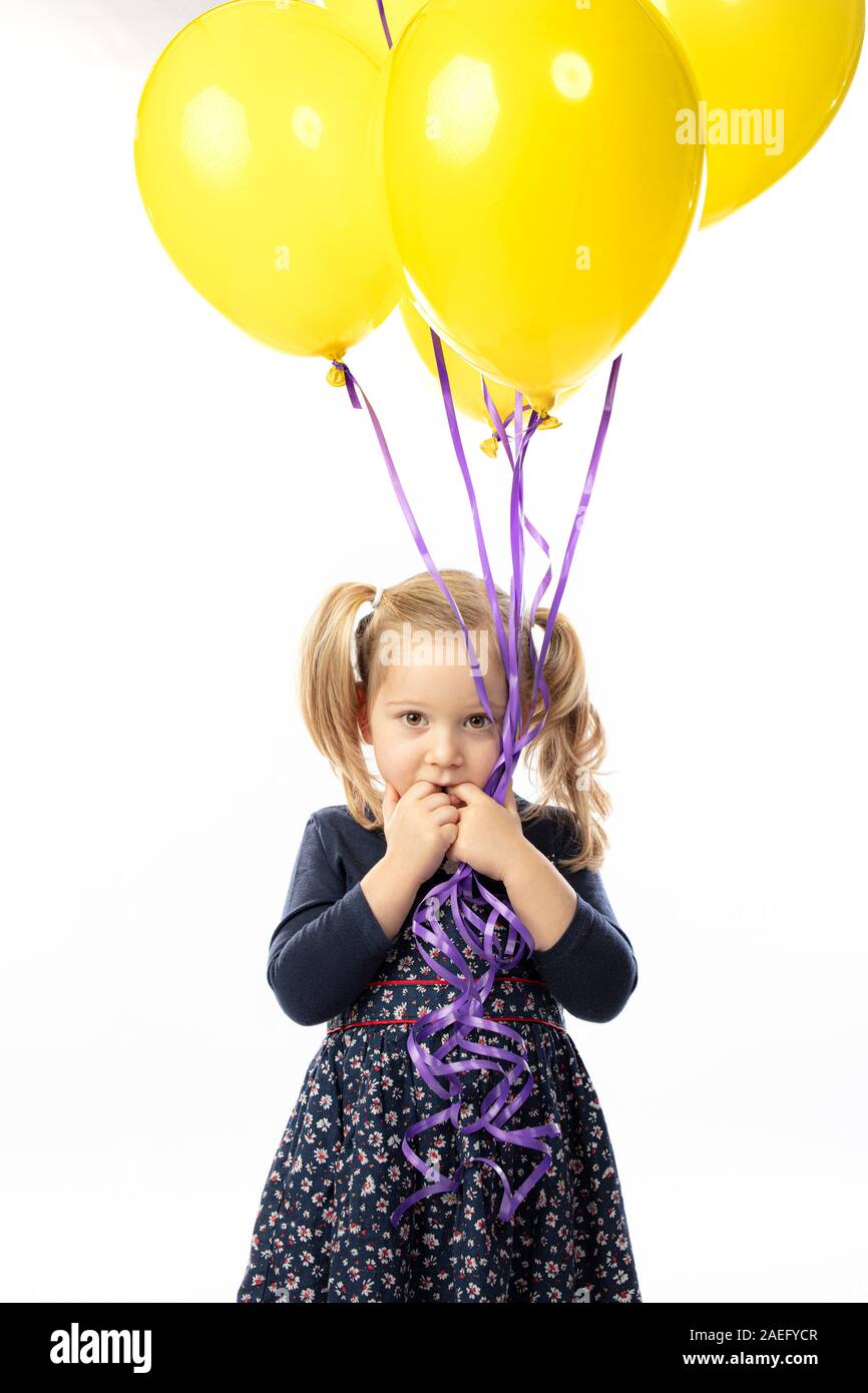portrait of a little blond girl holding yellow balloons. Concept of carefree and childhood. Stock Photo