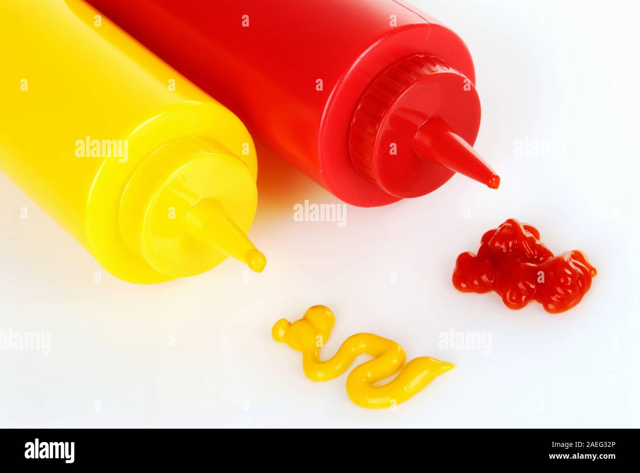 yellow plastic mustard bottle and a red plastic ketchup bottle are side by side. Each bottle has a swirly squirt of matching condiments. Stock Photo