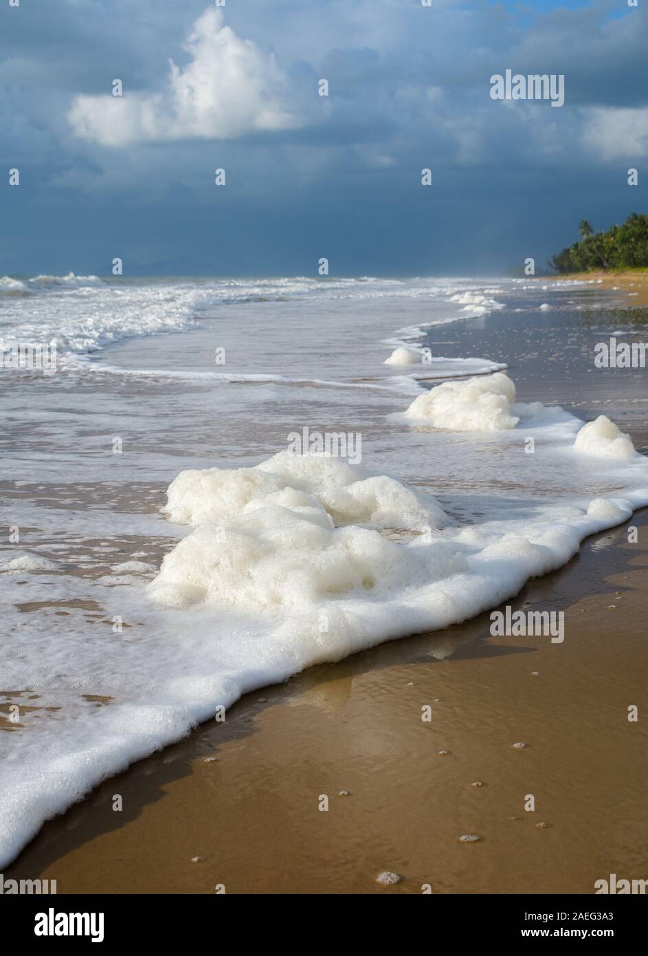 Foaming waves and tidal line leading to brooding storm clouds on Mission Beach in Queensland, Australia. Stock Photo