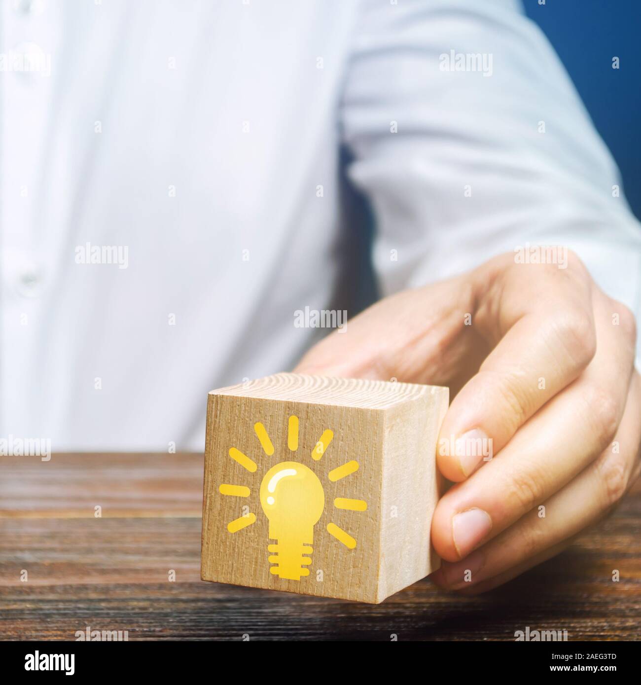 Businessman holds a wooden block with an image of a light bulb idea. Generation of innovative business ideas. Creative process. The accumulation of ex Stock Photo