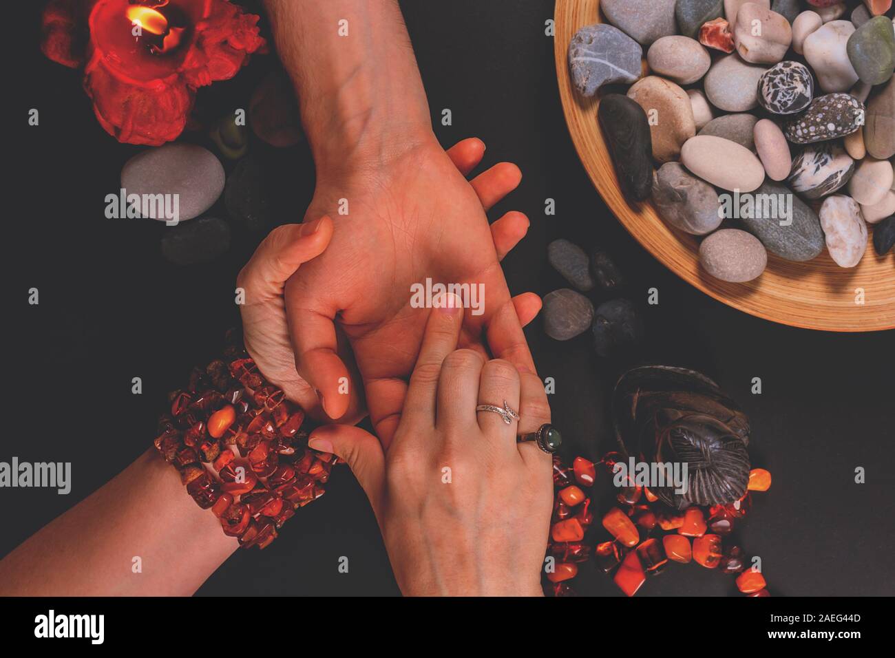 Young fortune teller divines the hand of young man around candles and other magical paraphernalia. Divine magic and occultism concept. Divination. Top Stock Photo