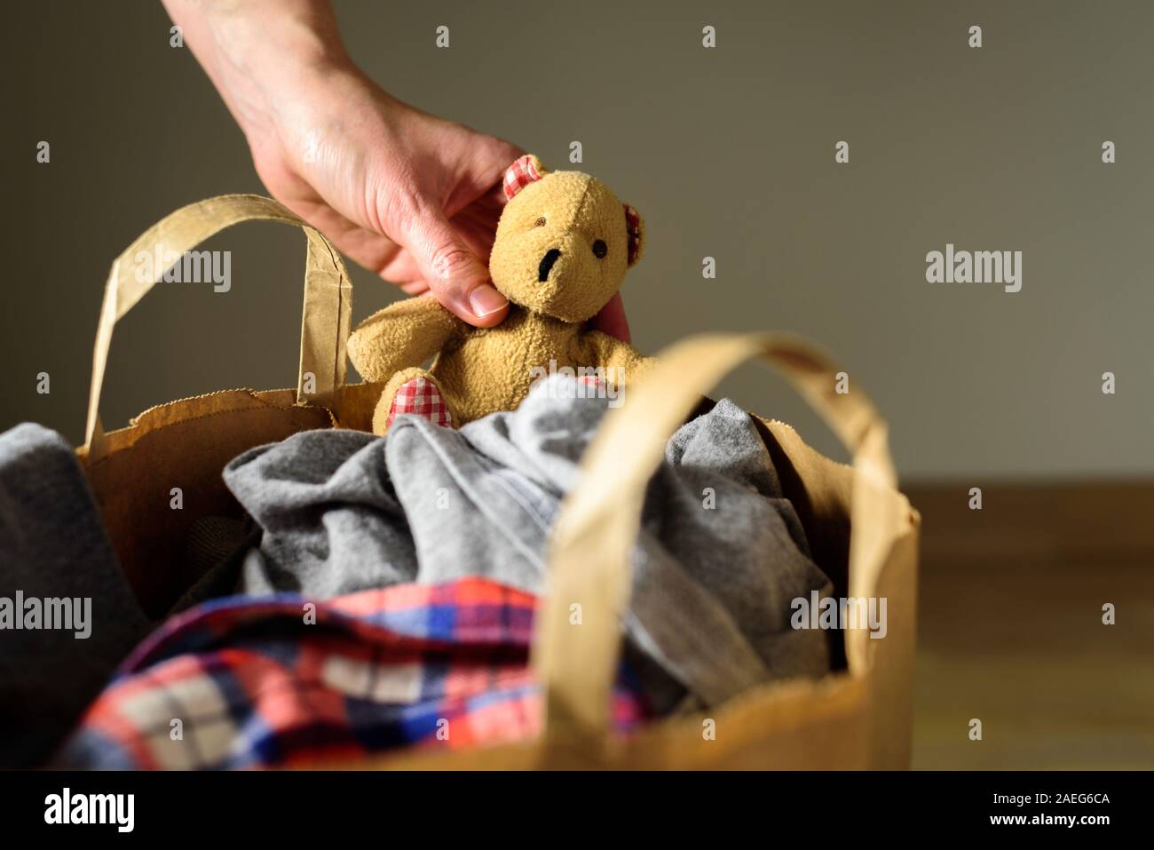 Paper bag with clothes donation. Old Bear toy in hand Stock Photo