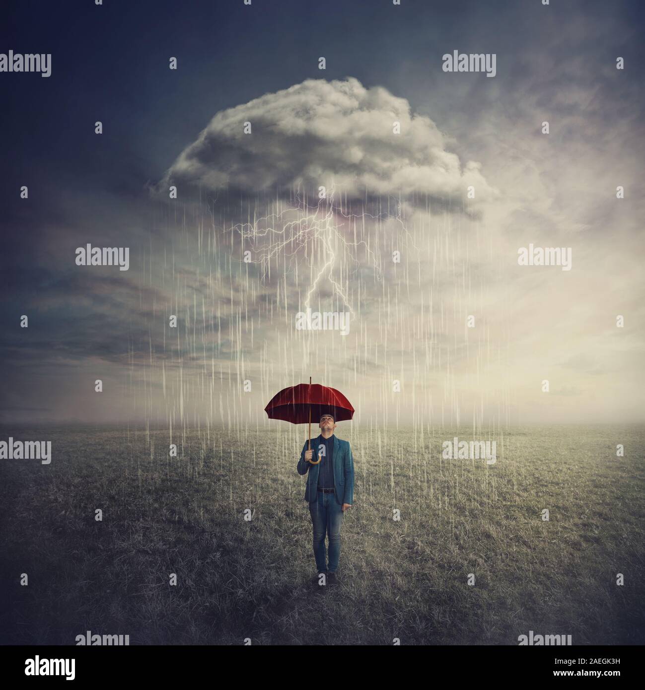Surreal scene as man stands outdoors under umbrella due a single mysterious storm cloud raining only over him. Find solution to escape crisis situatio Stock Photo