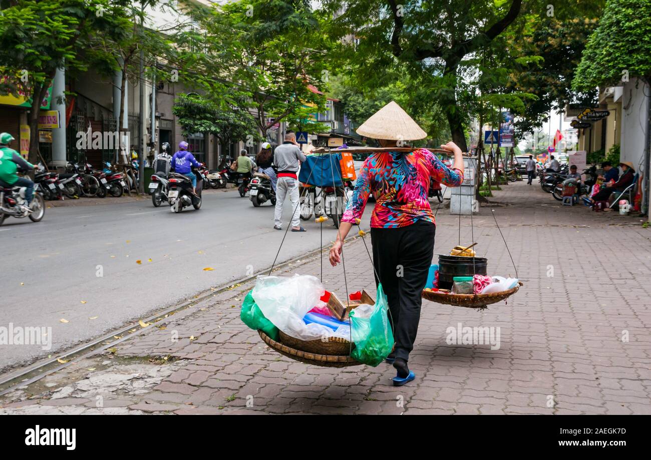Vietnamese woman wearing conical hat selling street food from baskets, Hanoi, Vietnam, Asia Stock Photo