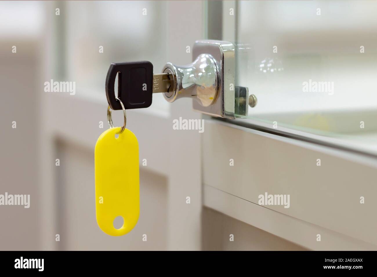 Lock with key with yellow tag on gray office glass furniture. Side view. Stock Photo