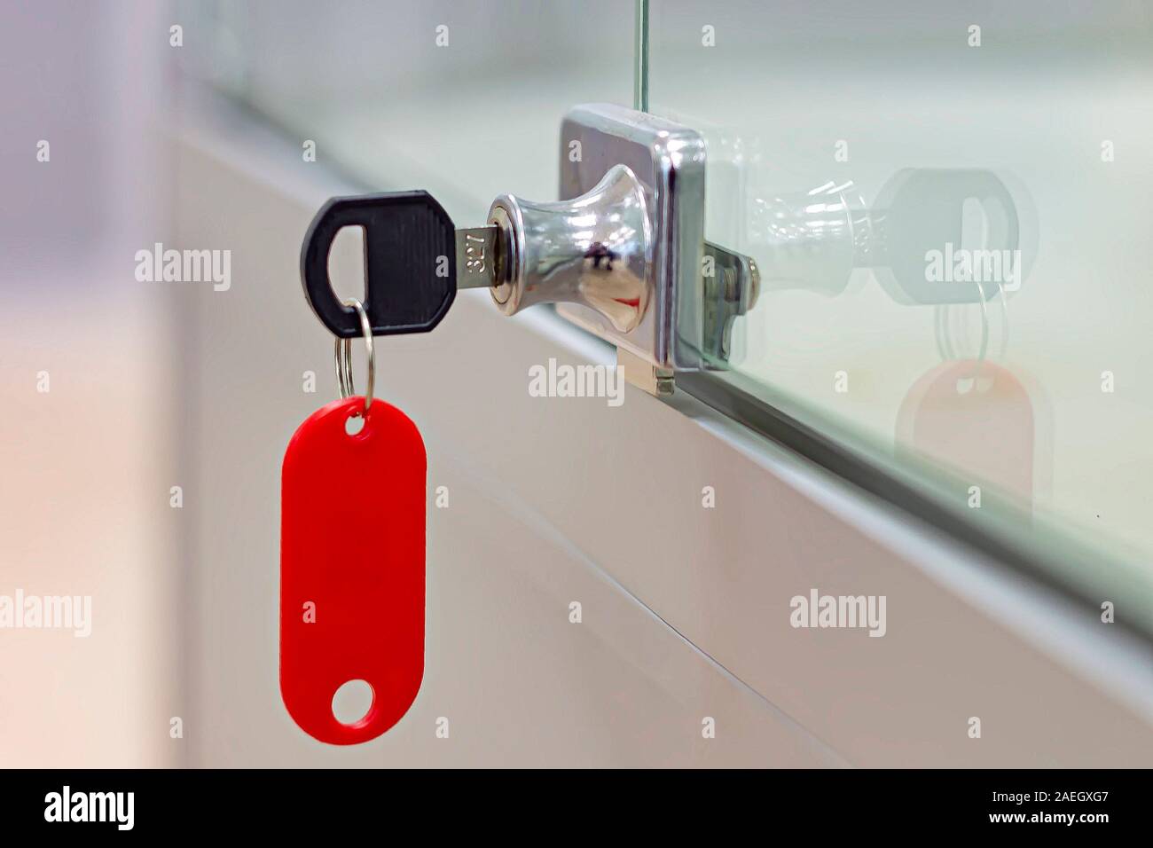 Lock with key with red tag on gray office glass furniture. Side view. Stock Photo