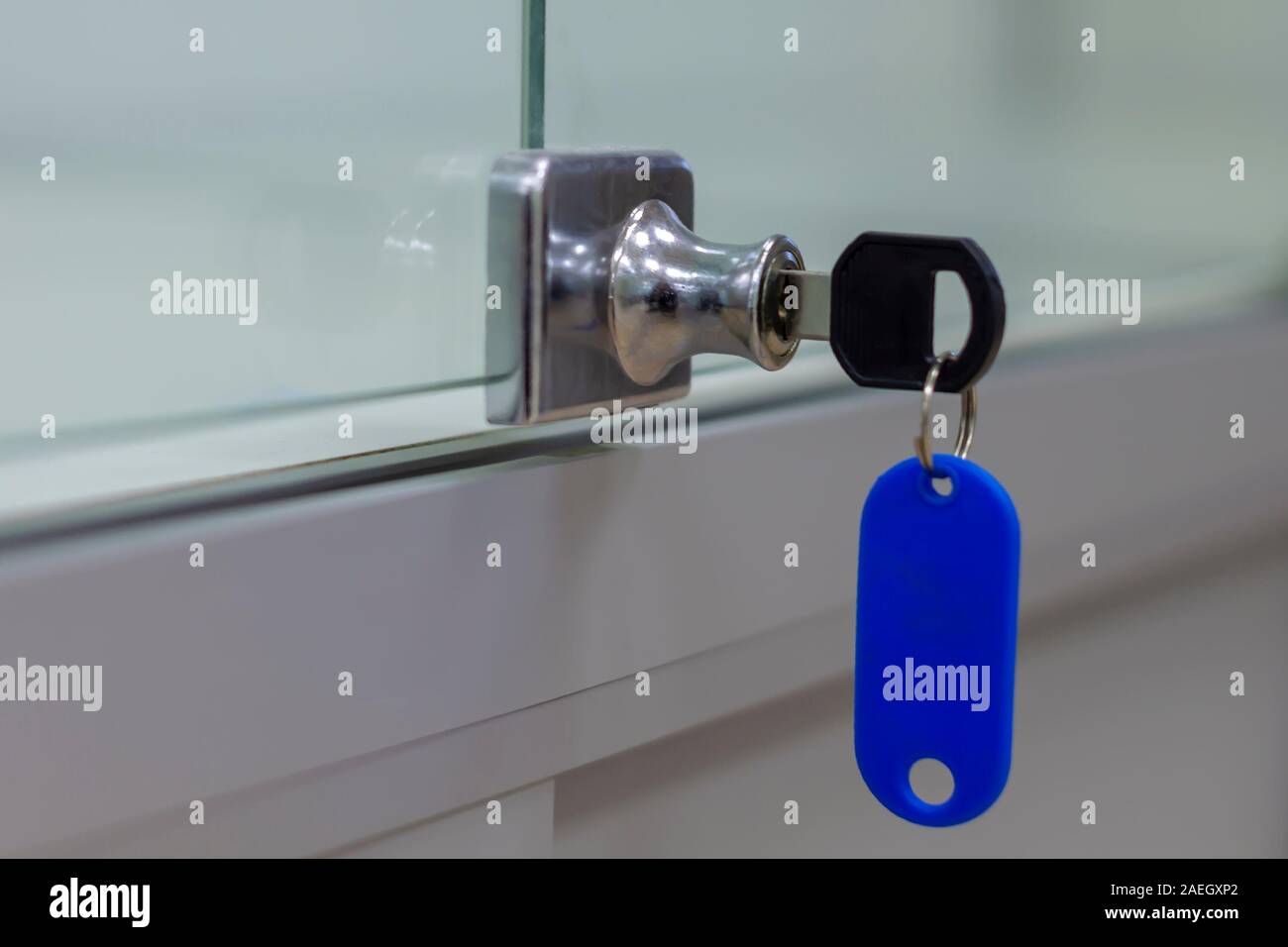 Lock with key with blue tag on gray office glass furniture. Side view. Stock Photo